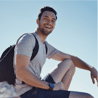 Anthony in athletic clothing and a backpack sitting on a rock