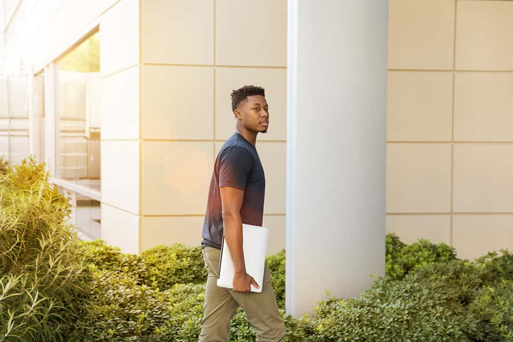 Student walking on campus and holding their laptop